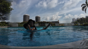 Child floating on a kickboard in a condo pool with the city skyline behind