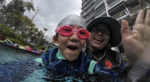 Two happy swimmers waving to the camera during a condo pool lesson